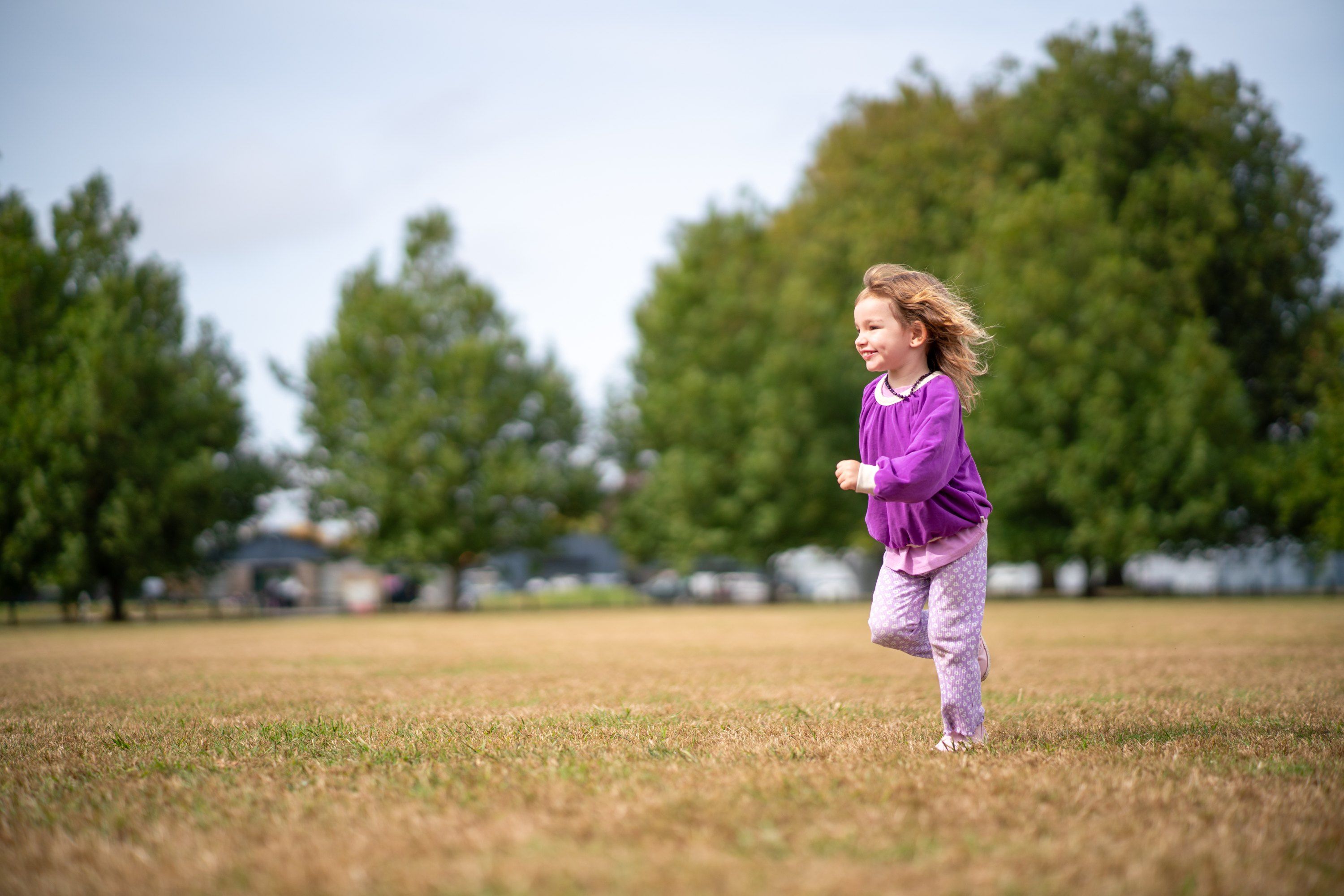 A preschooler in a purple jumper running across an open field, smiling